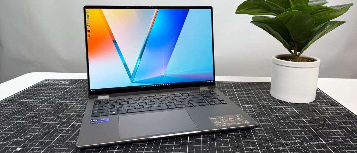 The Asus Vivobook 16 Flip convertible laptop on a black and white desk, against a gray background.