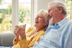 Elderly couple smiling while drinking coffee on the sofa