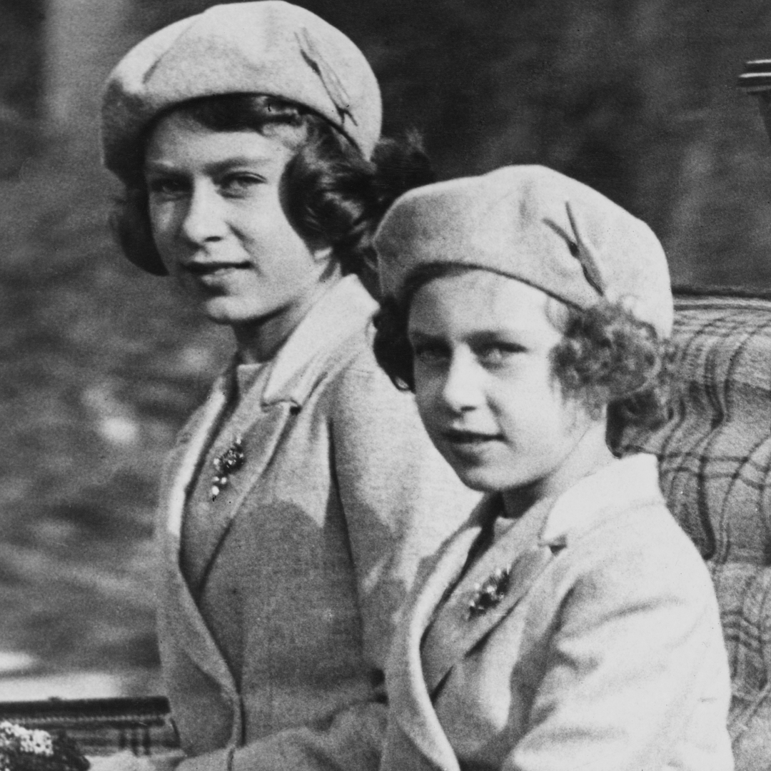 a black and white photo of Princess Margaret and Queen Elizabeth as children riding in a carriage wearing matching berets and coats