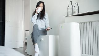 Does a dehumidifier cool a room? Image of woman sat next to a dehumidifier