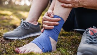 A hiker holds a bandaged ankle while sitting on the trail