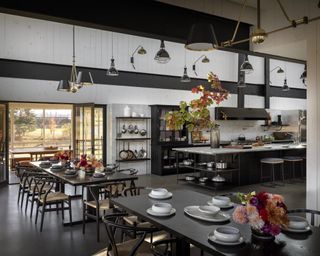 A large dining area with double height ceilings in a barn conversion with white walls and black furniture