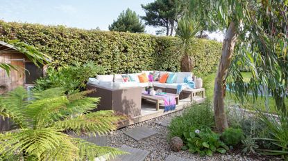 Sofa on a decked area beside a hedge, a gravelled area and lawn. 
