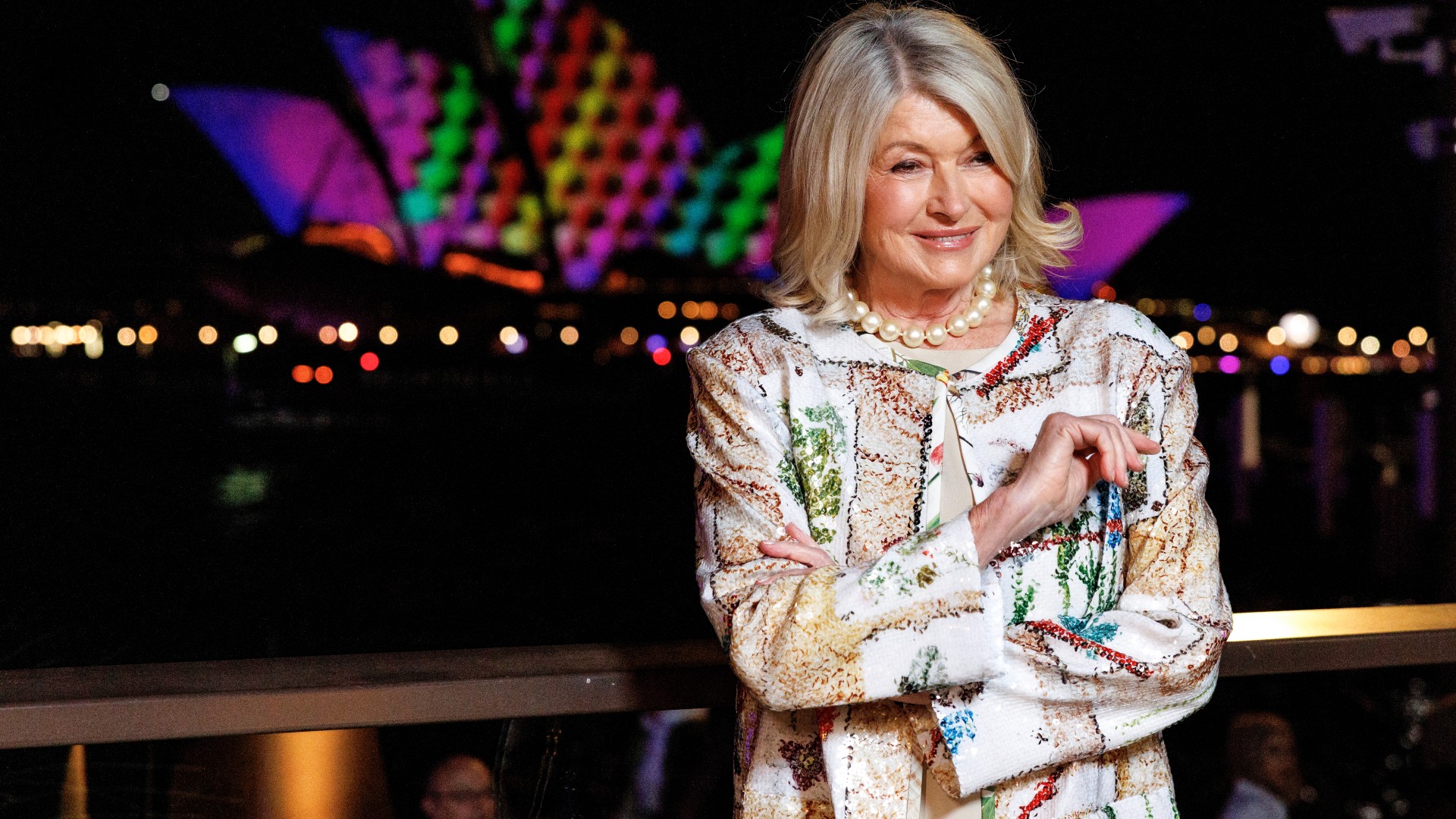 a white woman with short hair posing for a photo in front of the Sydney Opera House at night