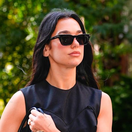 Dua Lipa wearing a black dress with heels and carrying an animal print clutch