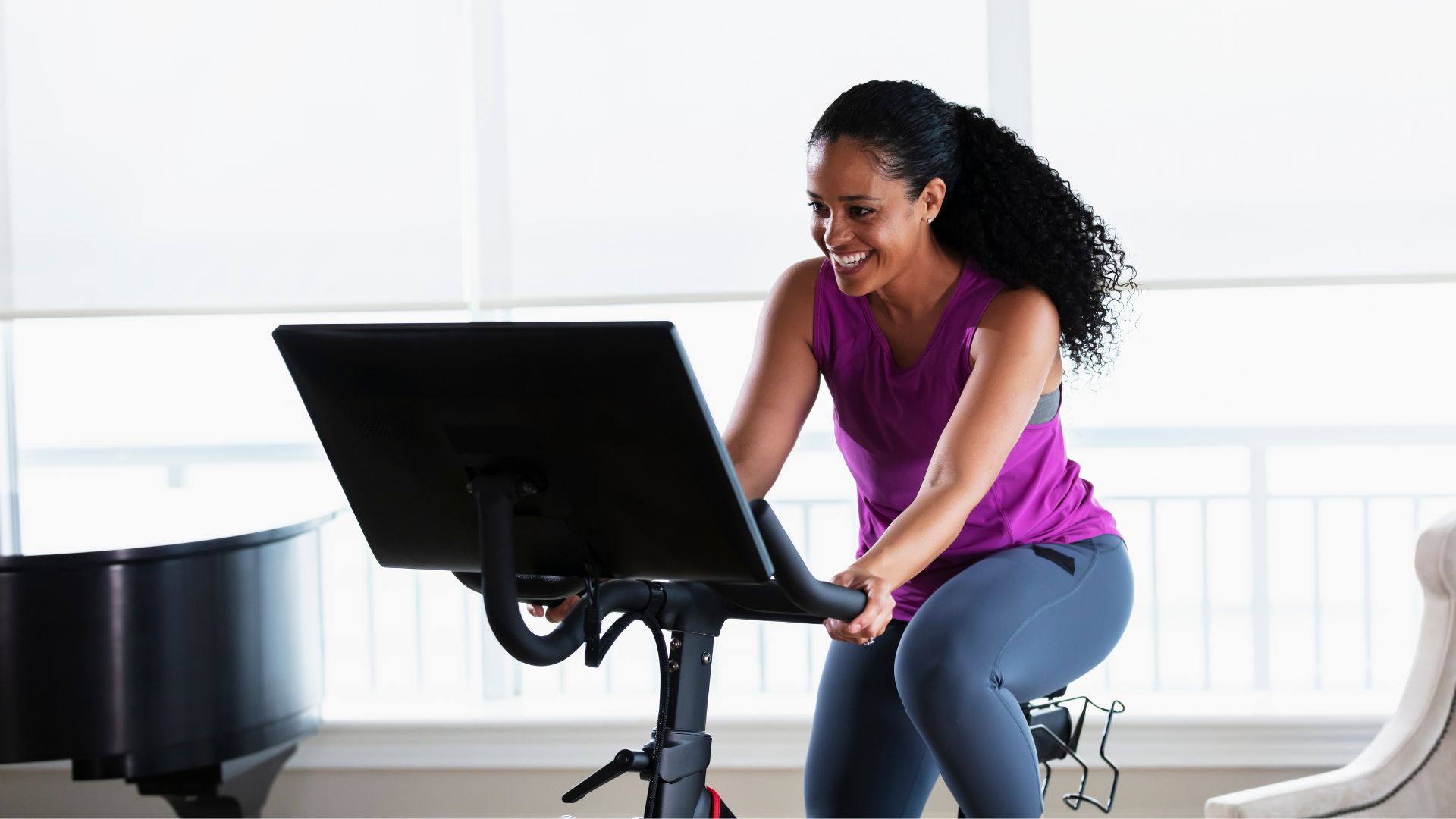 Woman riding on stationary bike indoors, smiling, doing cycling as a workout
