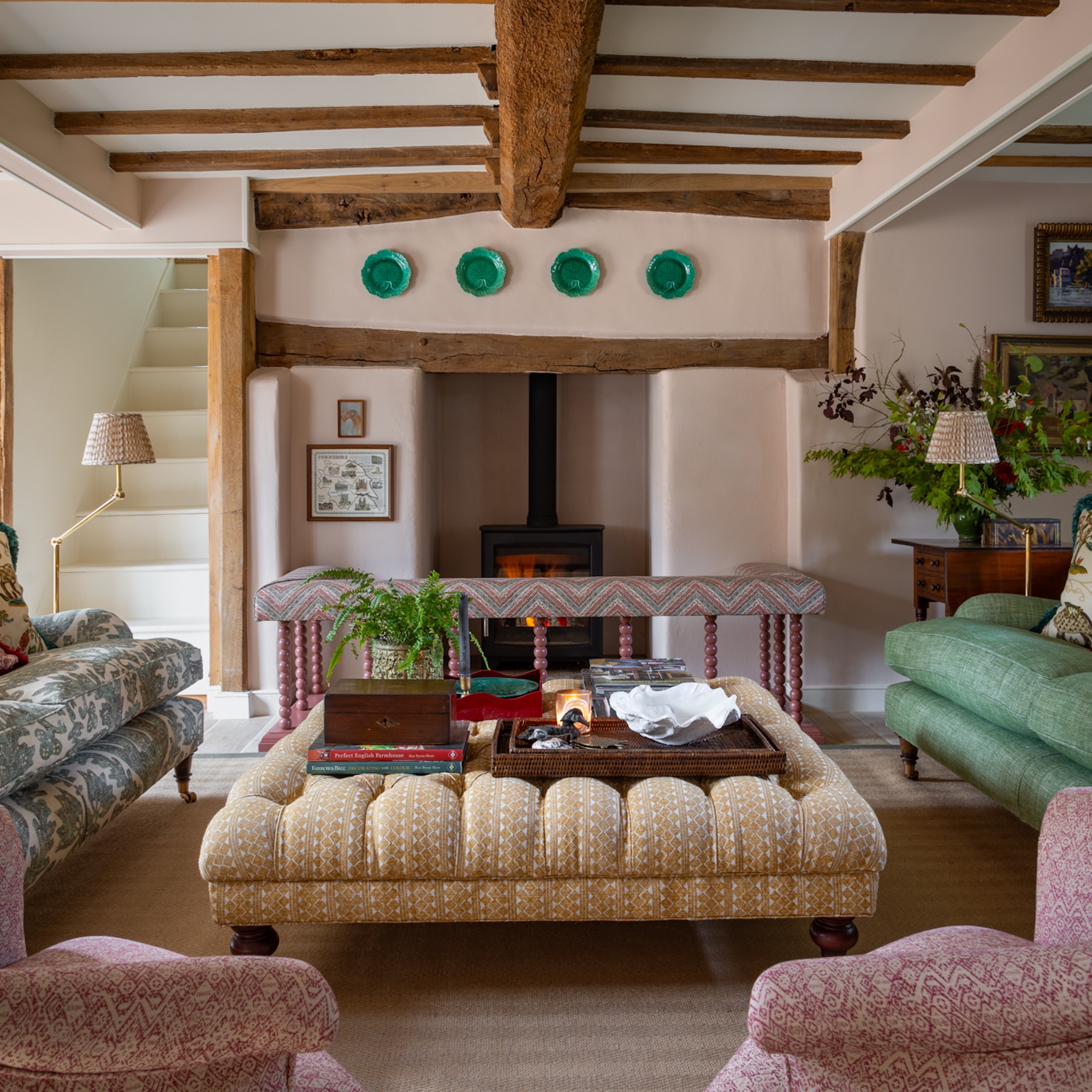 sitting room in English farmhouse with beamed ceiling, pink walls, large fireplace and upholstered furniture