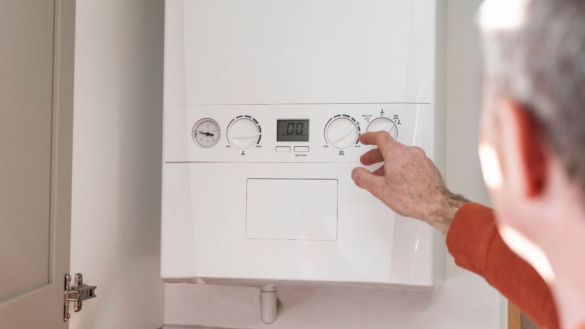 An over the shoulder shot of a mature male homeowner adjusting his boiler in his kitchen. The boiler is located in a cupboard.