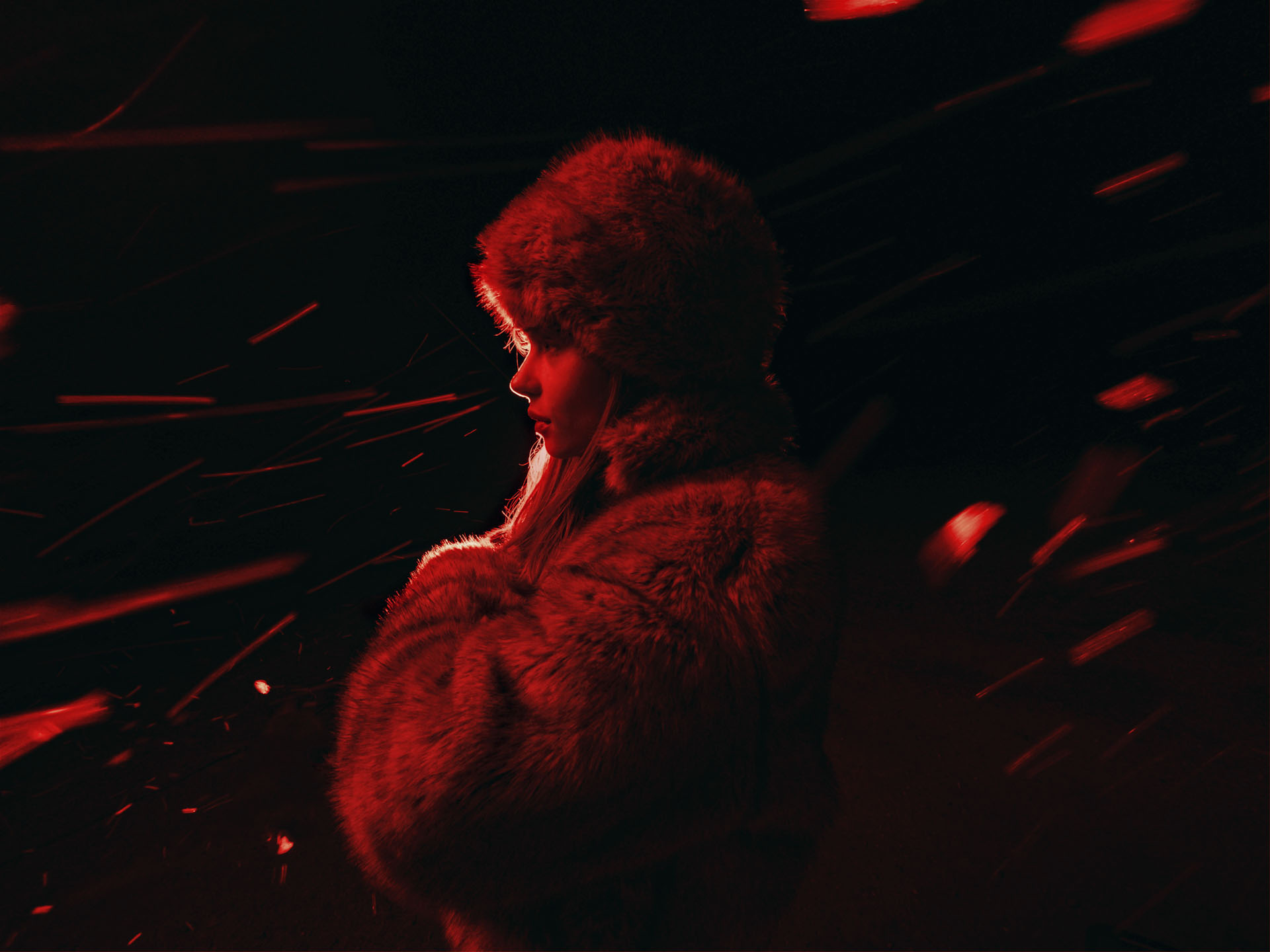 Female model in fur hat and coat in the dark, illuminated with a red light with sparks of light around her