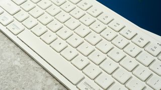 a super close close-up shot of a white wireless bluetooth keyboard resting on a clean white table