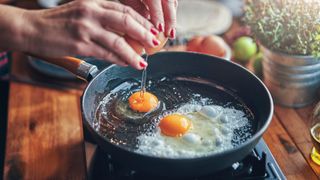 Woman's hands cracking two eggs into pan with oil, representing the low dopamine morning routine