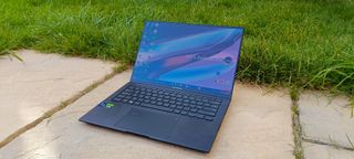 A black ASUS Zenbook Pro 14 OLED sitting on a patio in front of a grassy lawn