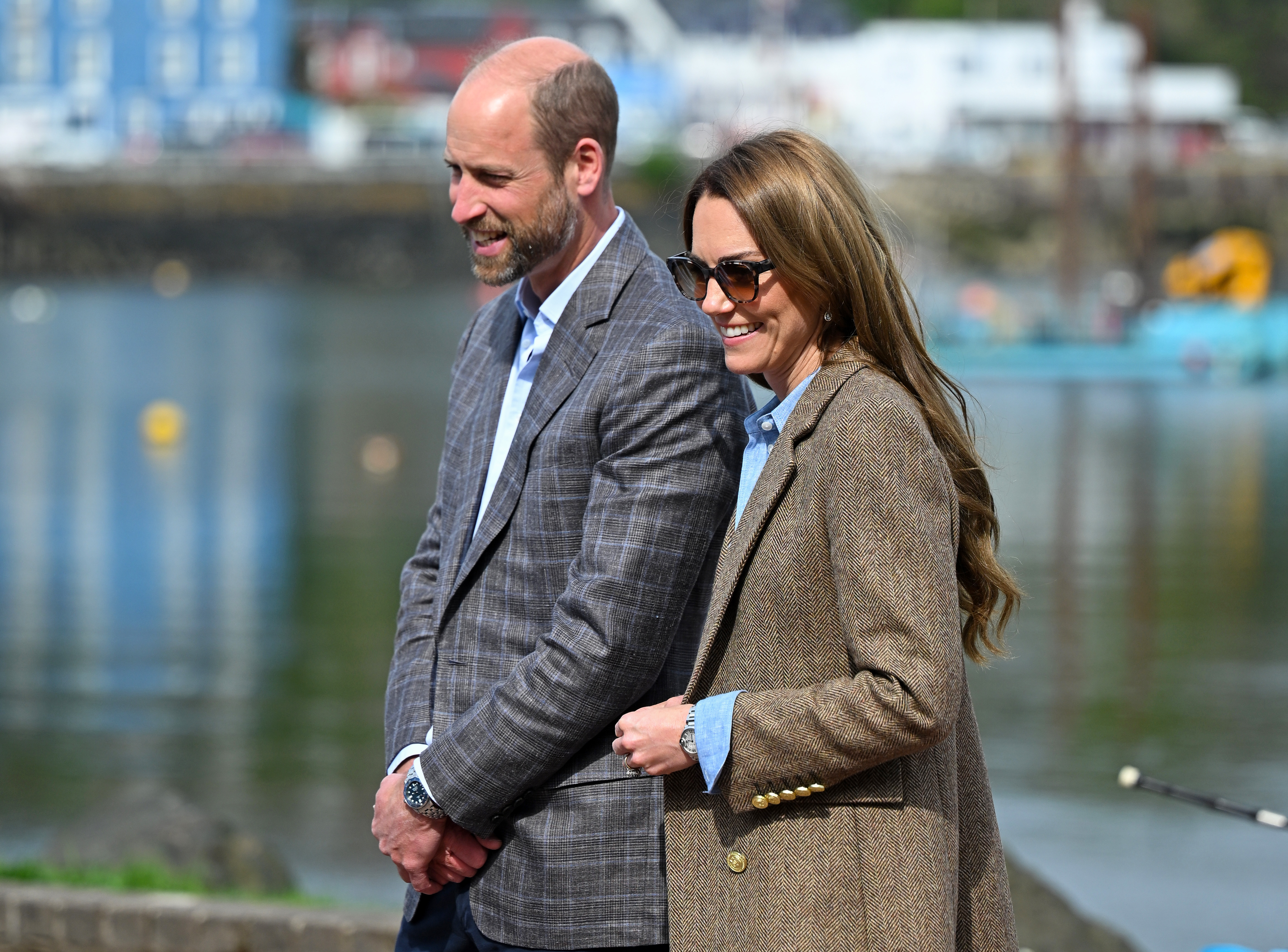 Prince William and Princess Kate smiling in front of a waterfront town