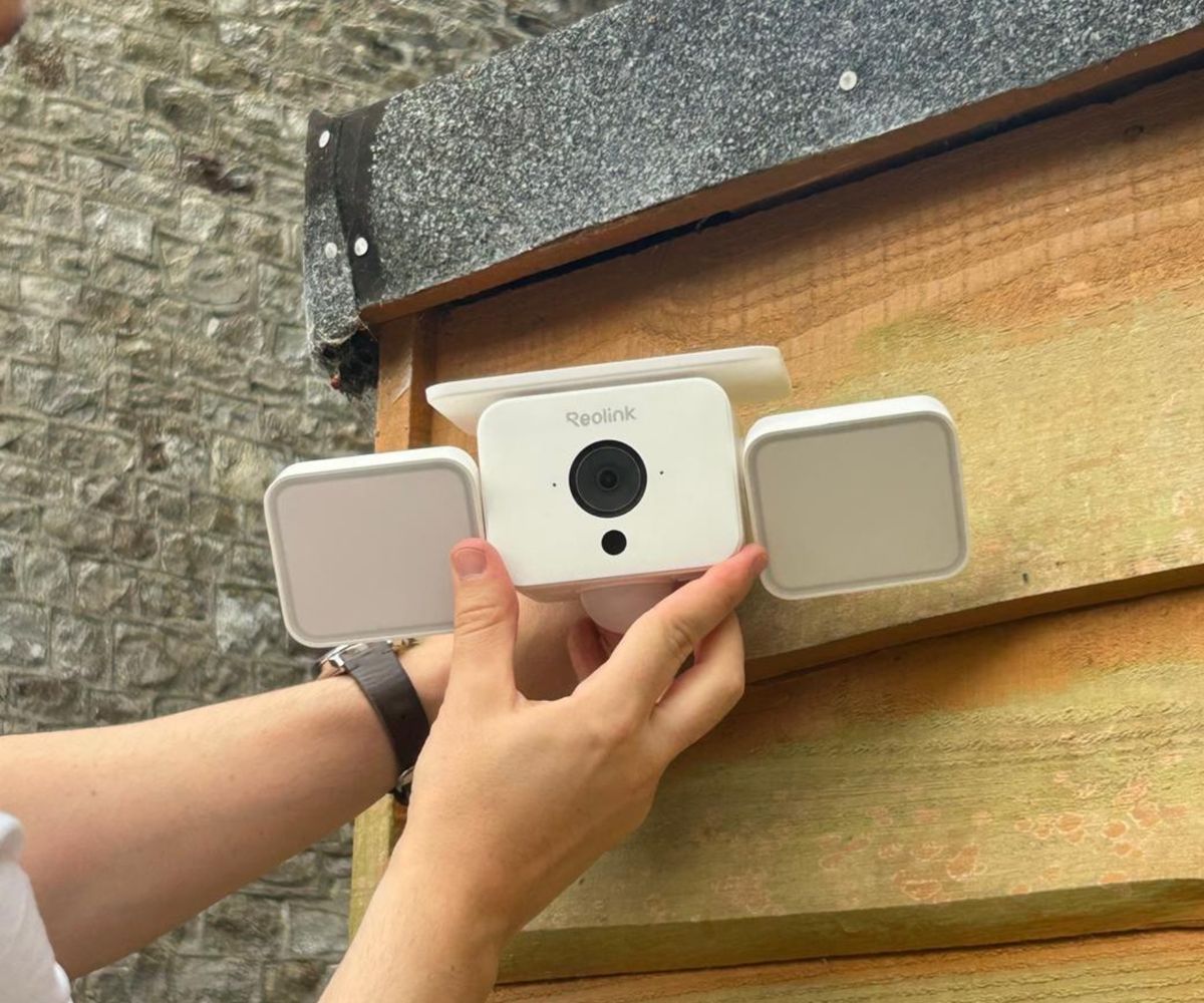 Hand holding Reolink floodlight camera against wooden fence post before fixing it in place.