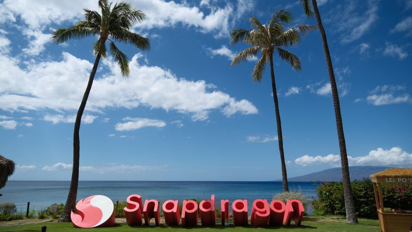 A Snapdragon sign beneath three gigantic palm trees with a blue sky and clouds in the background