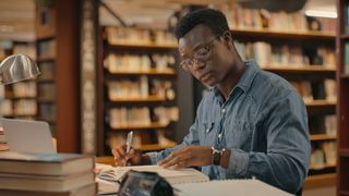 A male college student studies while sitting at a table in a library.