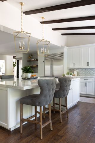 kitchen with white cabinets and island with white quartz worktops and dark wood floor plus grey upholstered stools and ceiling beams