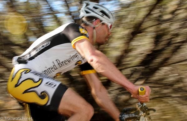 An Inspired Brewing rider streaks by the mesquite trees