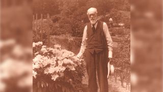 a sepia photograph of a man in old-fashioned clothes standing next to a flower bush