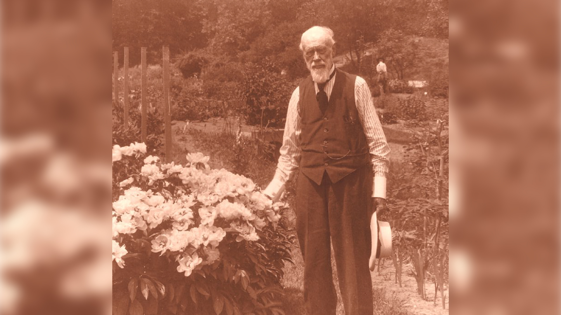 a sepia photograph of a man in old-fashioned clothes standing next to a flower bush