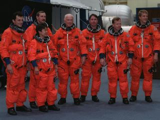 seven people wearing orange spacesuits are standing together.