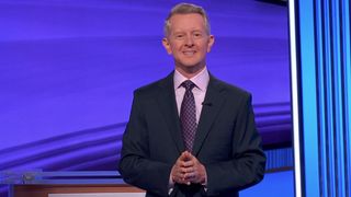 Ken Jennings at the beginning of an epsiode of Jeopardy, wearing a blue suit, pink shirt and blue and pink tie
