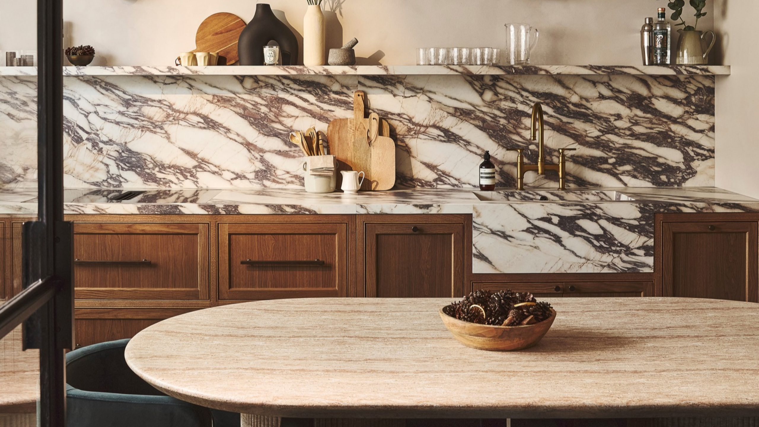Kitchen with veined marble counters and backsplash, wooden cabinets, and a dining table in the centre