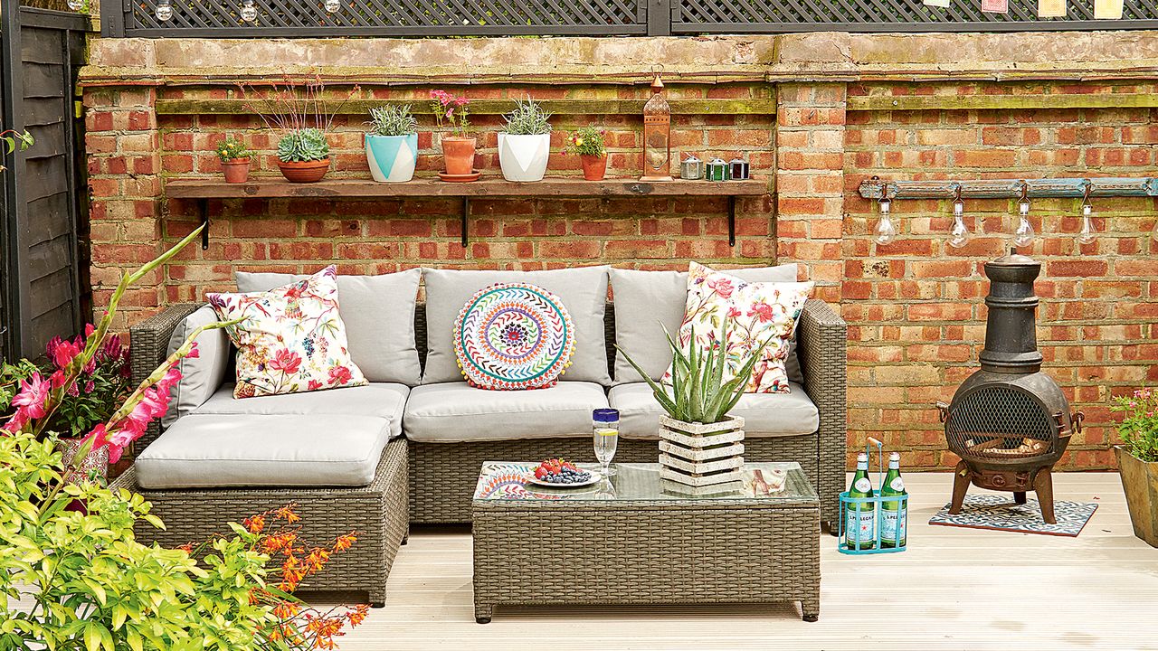 Red brick garden wall behind a corner sofa, decorated with accessories and lights