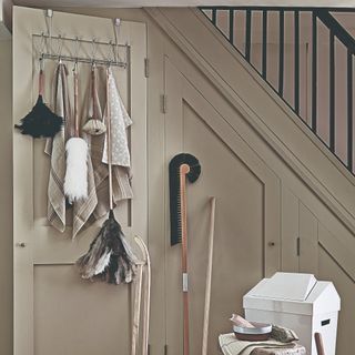 A hallway with an under-stairs storage unit for cleaning supplies and an over-door hanger