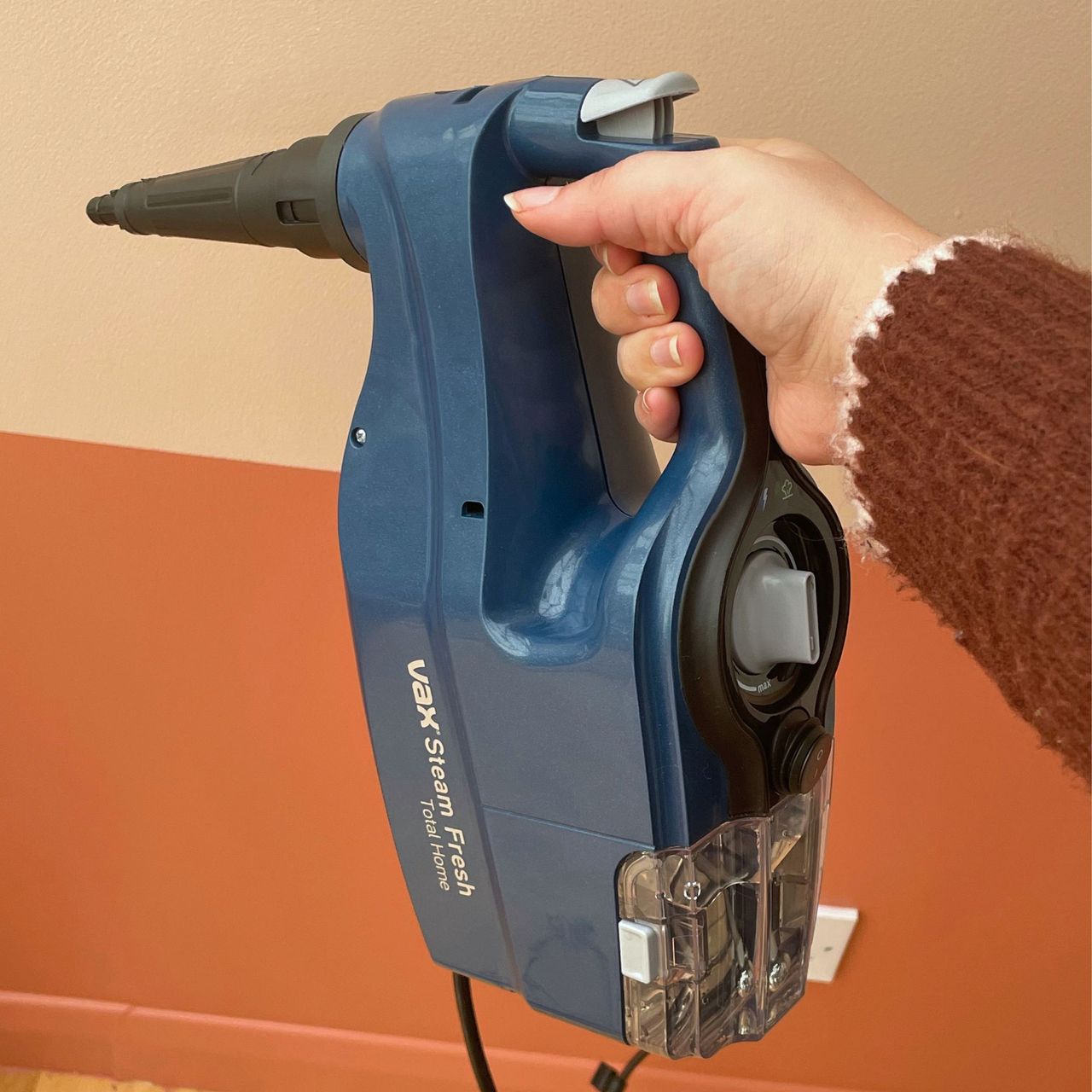 VAX Total Home Steam Cleaner being held in handheld form in front of a pink painted wall