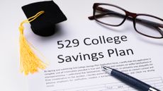529 College Savings Plan form with small graduation cap, spectacles, and a pen sitting on top of it
