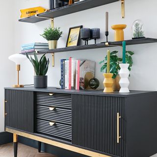 a black fluted sideboard with gold details and matching open shelving covered in art and displayed items