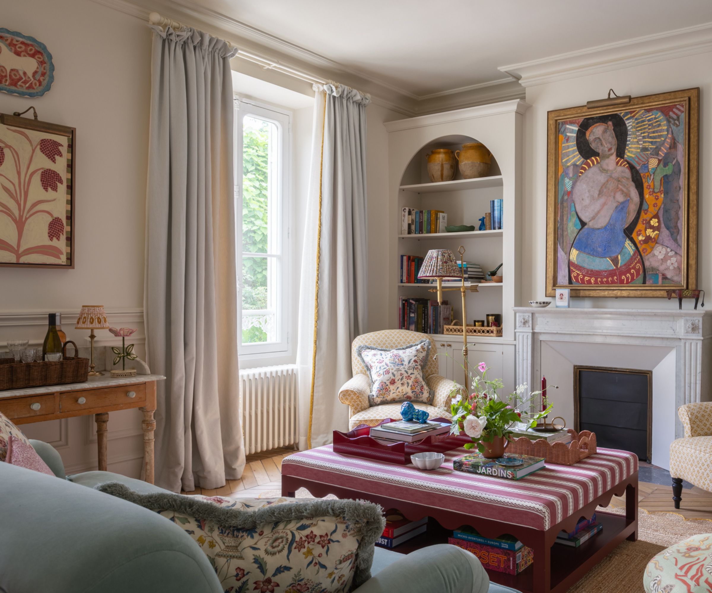 traditional living room with an eclectic mix of furniture, prints, and colors, a fireplace with large artwork and a striped ottoman