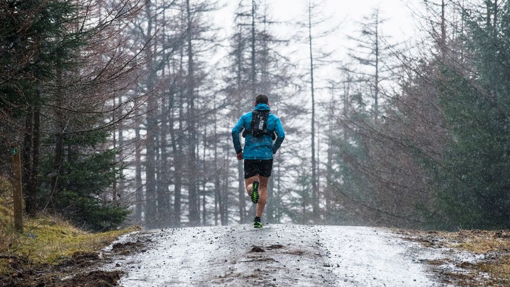 A trail runner runs along a wet trail