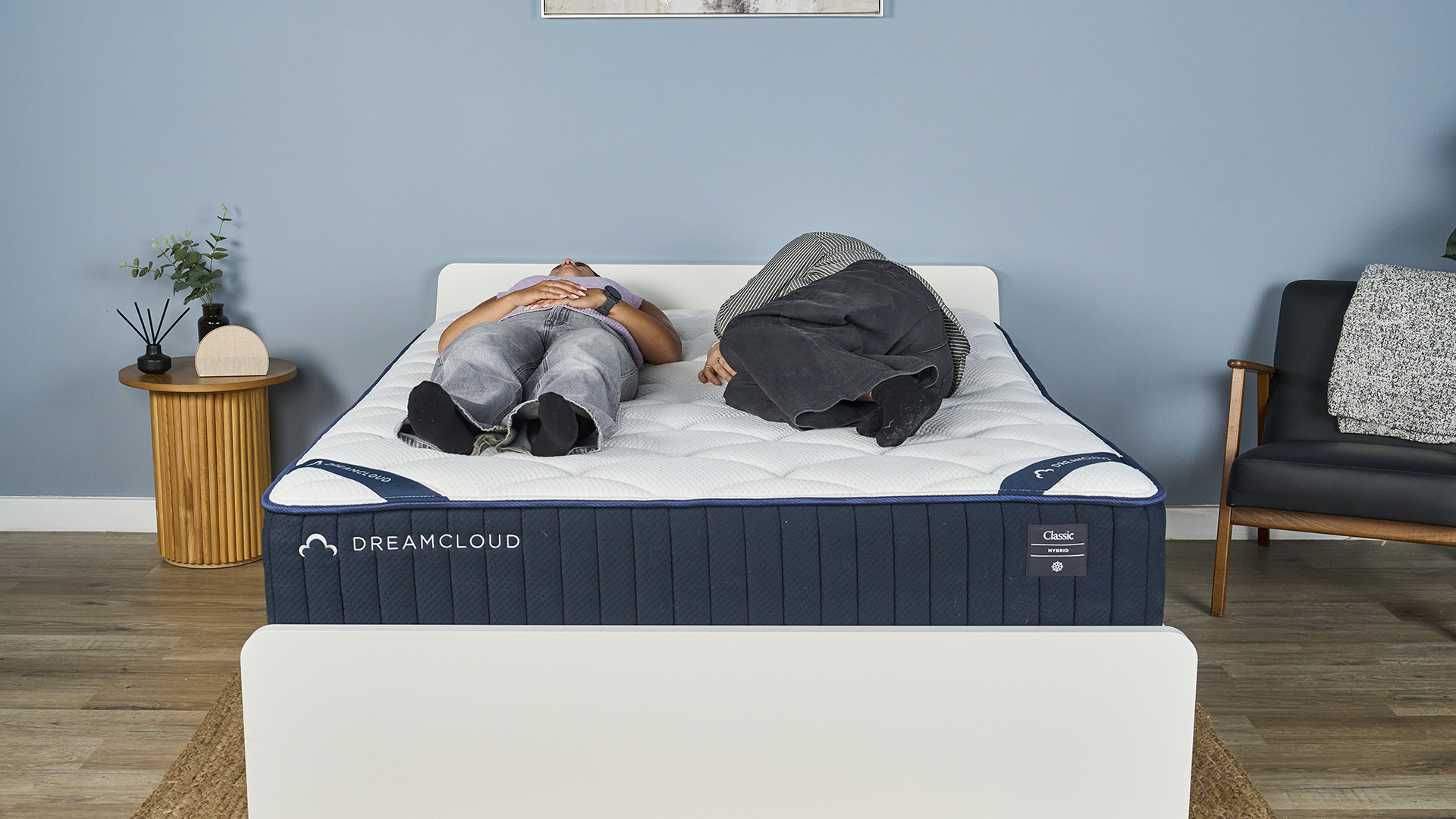 One Tom's Guide tester lies on her back on the DreamCloud Classic inside a blue-painted bedroom while another gets into bed, lies on her side and then lies on her other side