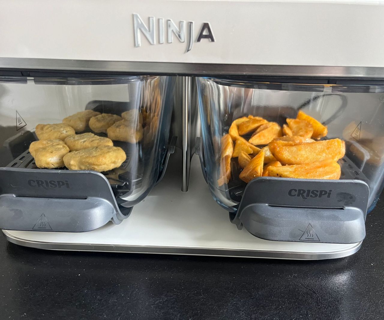 Two glass air fryer baskets with chicken nuggets in one and fries in the other viewed from the side.