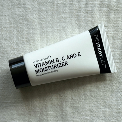 The INKEY List Vitamin B, C and E Moisturiser laying at an angle on an off-white linen background 