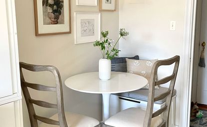 Small round dining table in corner space with gallery wall and white vase