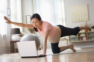 a pregnant mum practising pregnancy yoga online via a laptop
