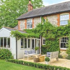 Cottage with a climbing plant all over it, with a large patio and patio furniture