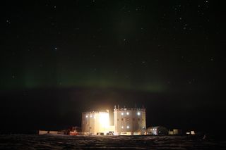 The white domes of the Concordia station photographed at night with aurora australis, southern lights in the sky.