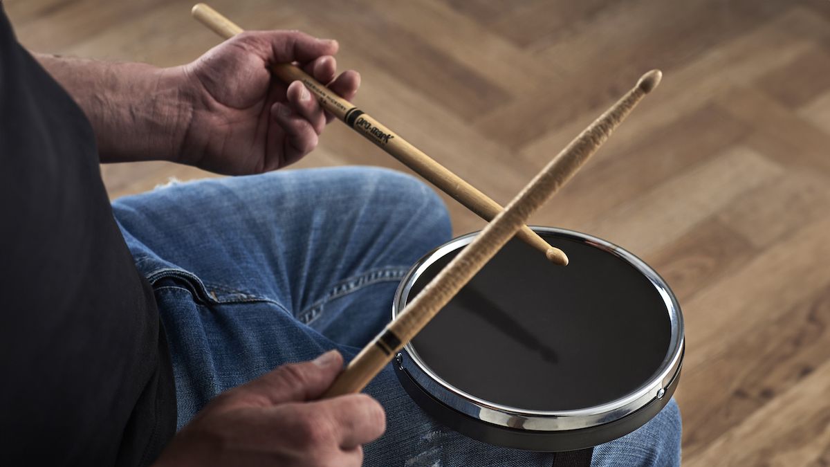 Man wearing black t-shirt and blue jeans plays a drum practice strapped to his knee