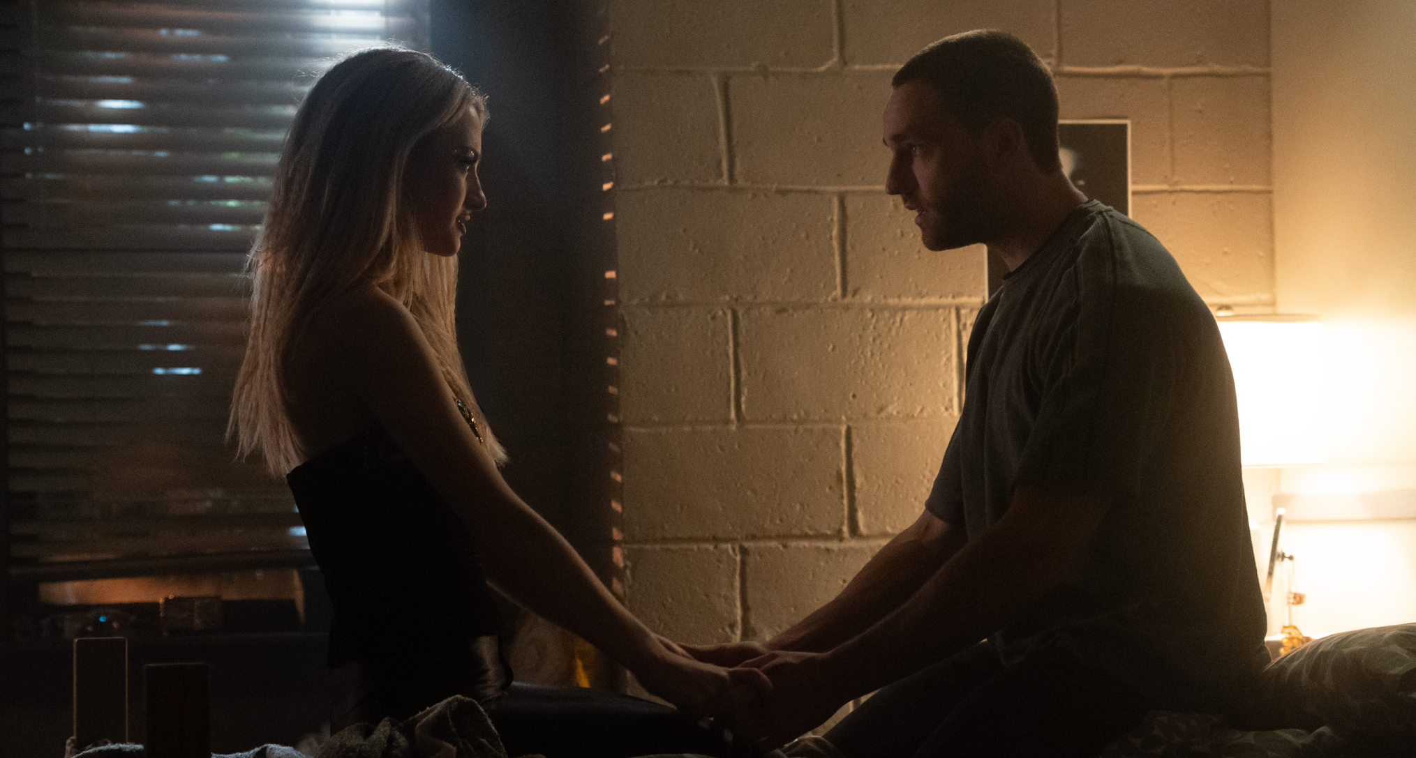 grace van patten as lucy and jackson white as stephen holding her hands while sitting on a dorm room bed in tell me lies season 3