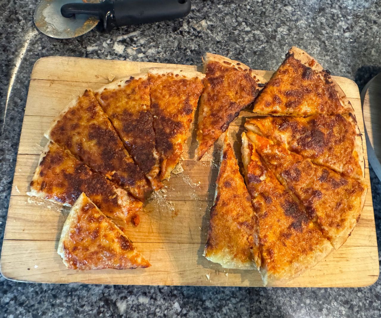 A toasted cheesy pizza on a wooden cutting board on a granite worktop