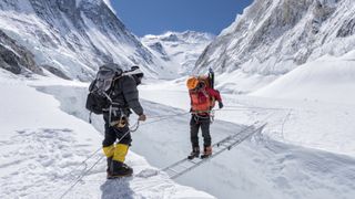 Two men cross a crevasse in a glacier using a ladder