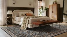 Warm, richly layered bedroom featuring a sculptural cream bed frame, terracotta iron ottomans, and a moody floral rug.