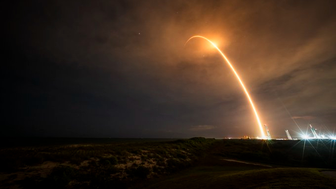 A rocket launch carves an orange arc into a dark night sky in this long-exposure photo.