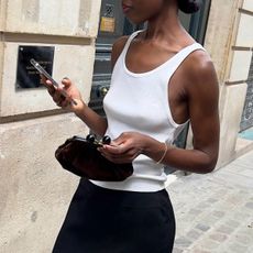 @sylviemus_ outfit shot in white tank with black skirt holding phone 