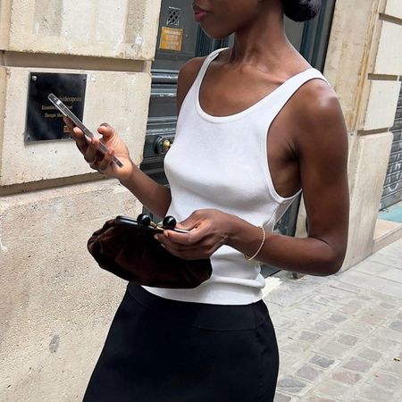 @sylviemus_ outfit shot in white tank with black skirt holding phone 