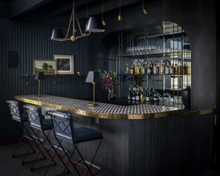 A home bar with deep-blue green walls, walnut panelled bar and mirrored back bar